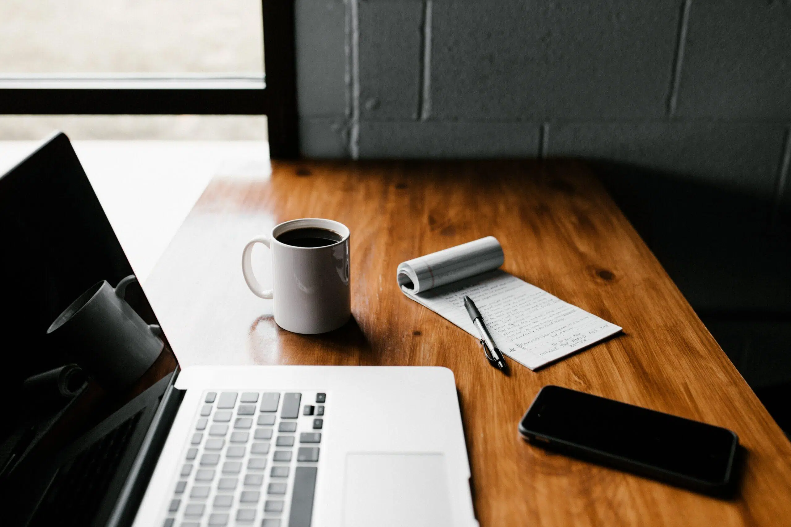 Desk with a notebook, coffee, mug and a laptop