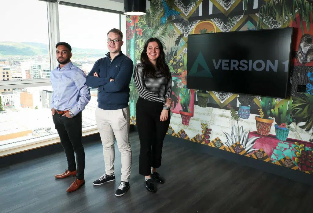 3 people in a modern office with Version 1 on screen behind them