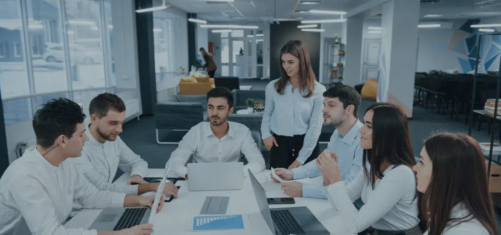 Seven people around a table in an office with laptops and documents