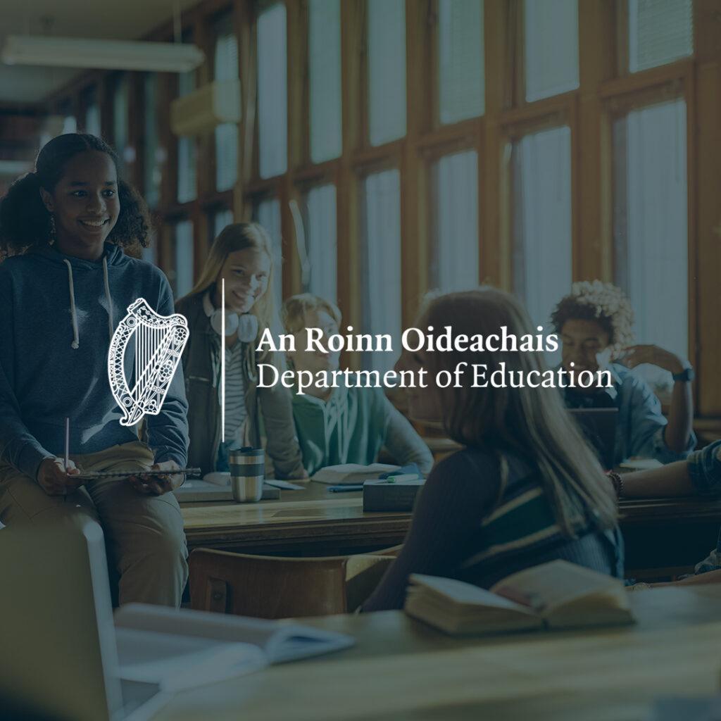 An-roinn-oideachais. Department of Education logo over an image of people in a school classroom