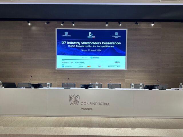 A desk with chairs behind it for speakers to sit at for a panel discussion. Screen in background that reads 'G7 Industry Stakeholders Conference'