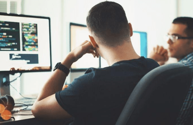man sat at his desk in front of a computer monitor. seen from behind