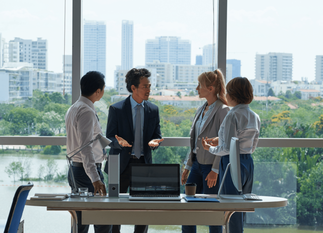 A professional team engaged in a collaborative discussion in a modern office setting, with a cityscape visible through the large window, highlighting a contemporary work environment.