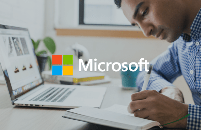 Microsoft logo over an image of a person writing in a notebook with his laptop on his desk