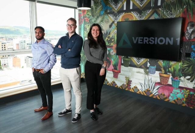3 people in a modern office with Version 1 on screen behind them