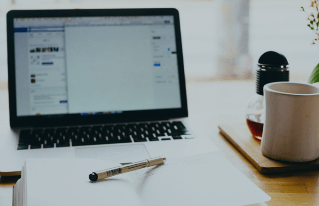 laptop on desk with pen, notebook and coffee