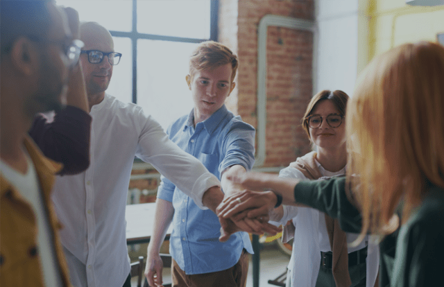 Five people placing their hands together in the centre