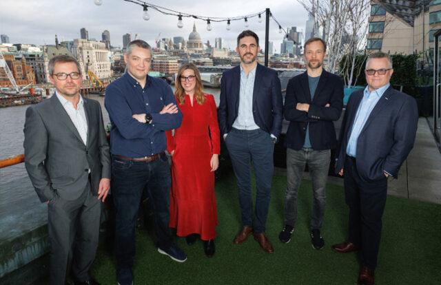 Six people stood on a balcony in front of a river