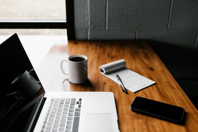 Desk with a notebook, coffee, mug and a laptop