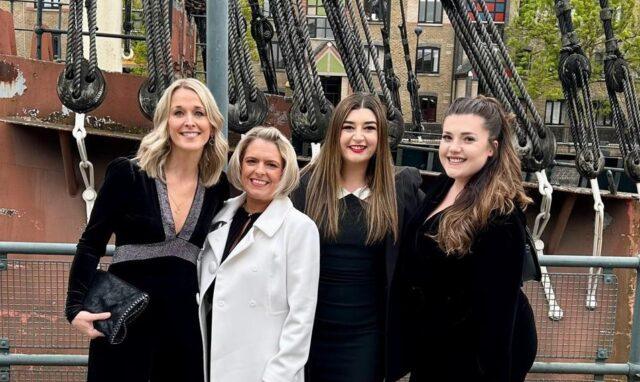 Four women dressed smartly stood in front of a boat