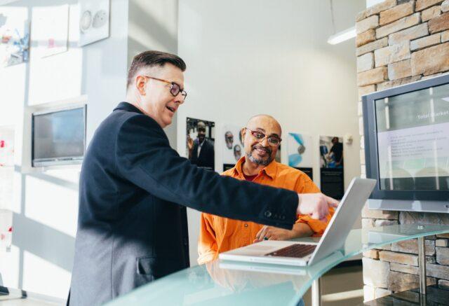 Two men at a laptop smiling