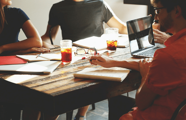people sat at table with books and laptops