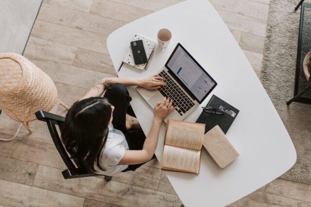 overhead view of a person sat at a desk with laptop and book, phone and coffee