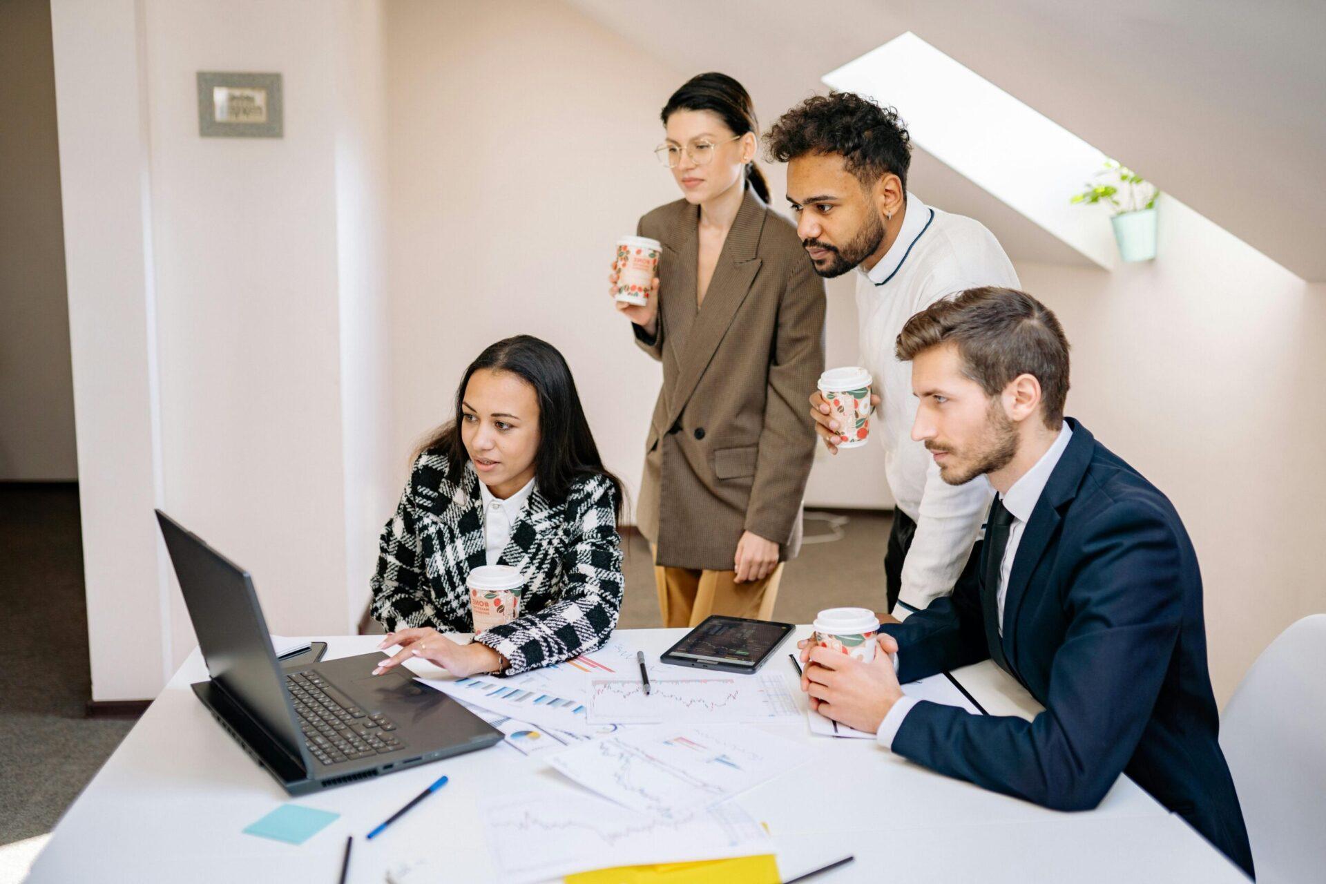Four people around a laptop with coffees