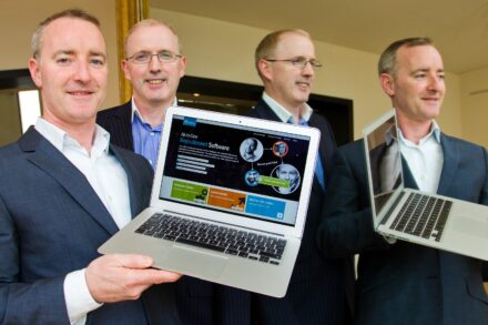 Four men in suits holding laptops smiling