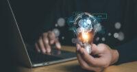 hand holding light bulb with digital imagery icons representing AI overlaid