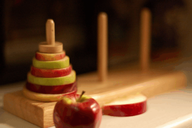 A tower of Hanoi puzzle with stacked apple rings with an apple in the foreground.