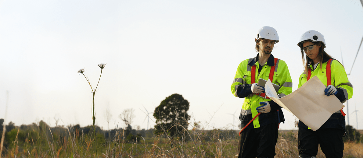 Two people in high-vis jackets, looking at plans, standing in front of a windmill