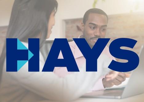 A large blue Hays logo is displayed over a scene of two people sitting at a desk, engaged in a conversation while looking at a laptop.