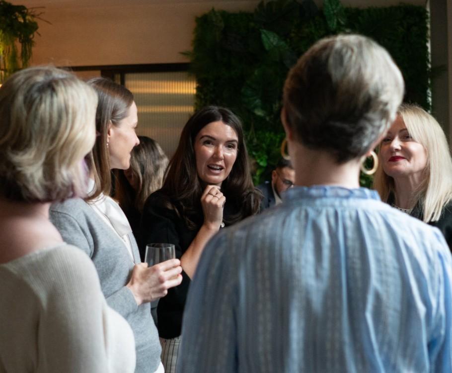 Becki Pedley hosting a fireside chat at Version 1’s Women in Tech Leadership event, with a group of women networking and chatting in a relaxed indoor setting. AI leadership insights.