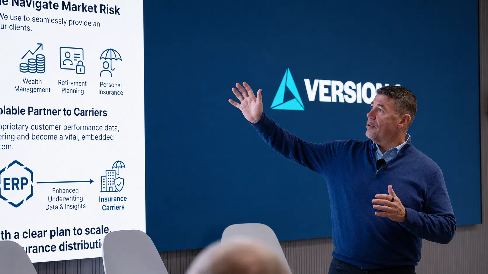Man presenting in a modern conference room, gesturing toward a large screen displaying financial services icons and text, with a corporate logo on a blue background behind him