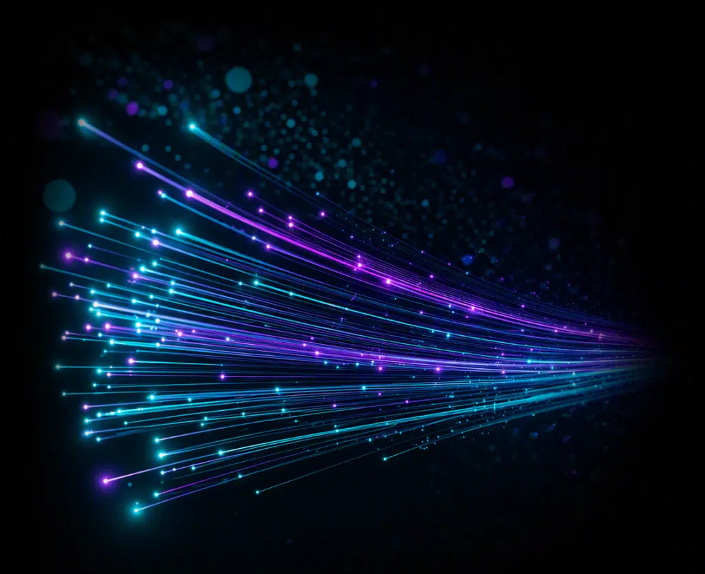 Abstract digital illustration of glowing blue and purple fibre-optic light trails streaming across a dark background. Bright points of light travel along curved lines, creating a sense of speed, connectivity, data transfer, and high-tech communication. The edges fade into black, with scattered bokeh-style light particles adding depth and motion.