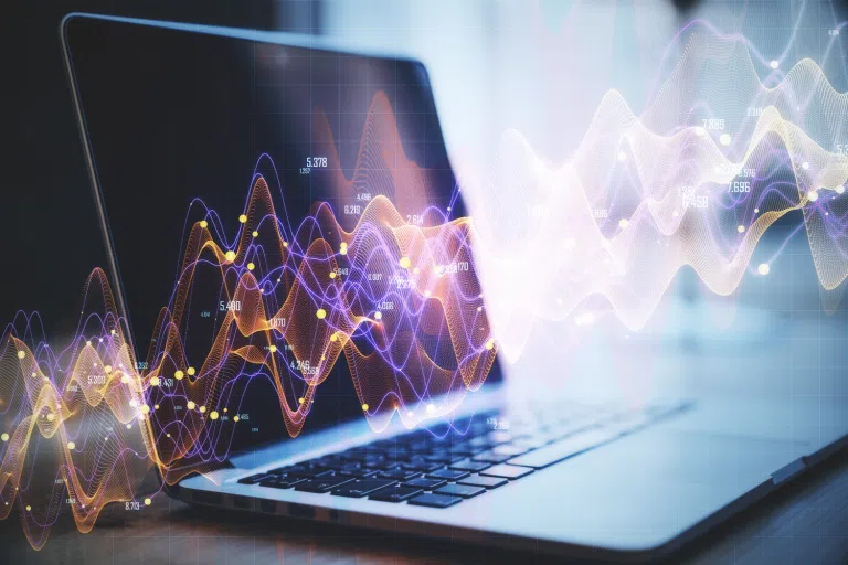 Laptop displaying advanced data visualisation graphics with colourful wave patterns, data points and numerical overlays representing analytics, artificial intelligence or machine learning processes. Abstract digital signals flow across the screen against a blurred technology-focused background.