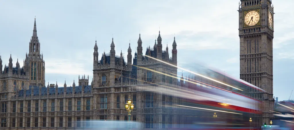 Big Ben and the Houses of Parliament in London, with a passing red double-decker bus, representing UK government, public sector and transport infrastructure.