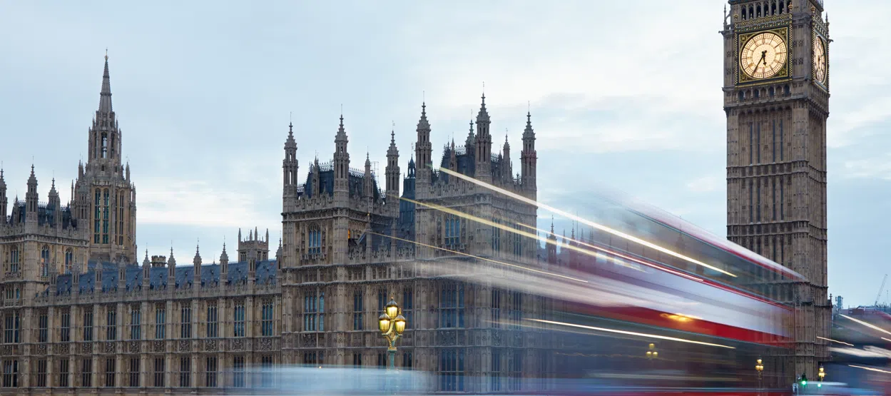 Big Ben and the Houses of Parliament in London, with a passing red double-decker bus, representing UK government, public sector and transport infrastructure.