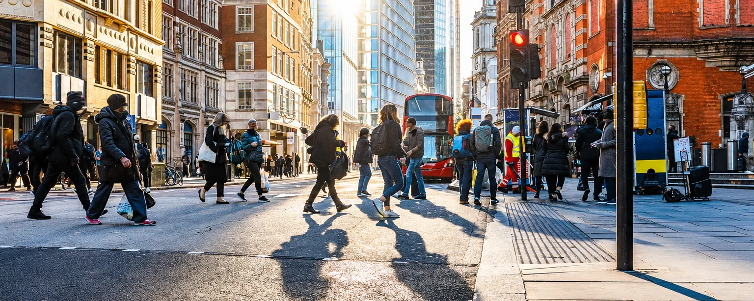 People crossing a busy London city centre street with a red double-decker bus and commercial buildings, representing urban infrastructure, public services and business transformation in the UK.