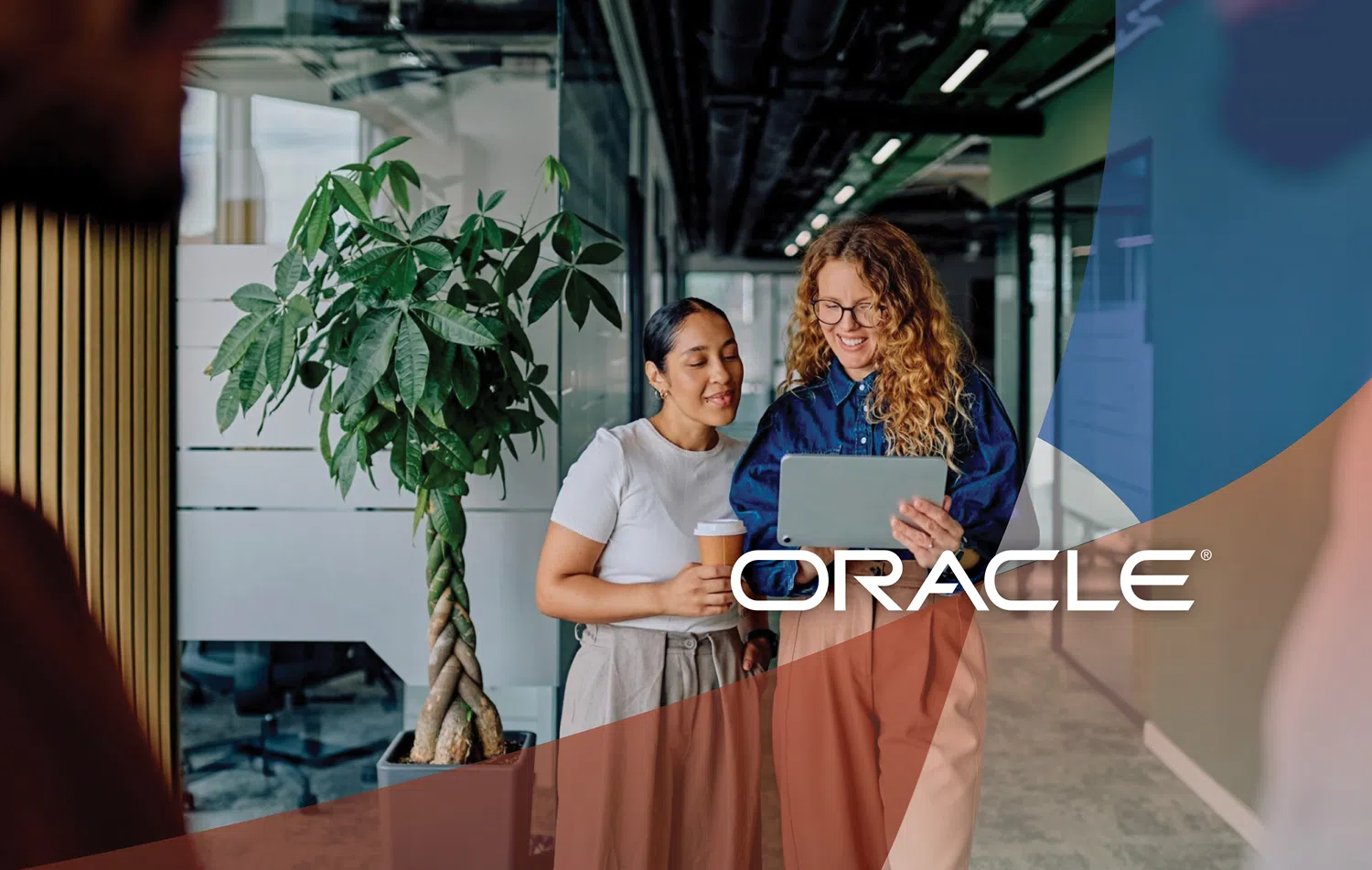 Two professionals standing in a modern office corridor reviewing content on a tablet device beside a large indoor plant, with Oracle branding and abstract blue graphic overlays in the foreground.